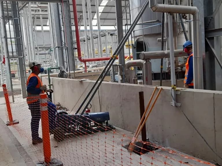 Profissionais executando a Microestaca Arcos com equipamento compacto entre as tubulações de uma instalação industrial