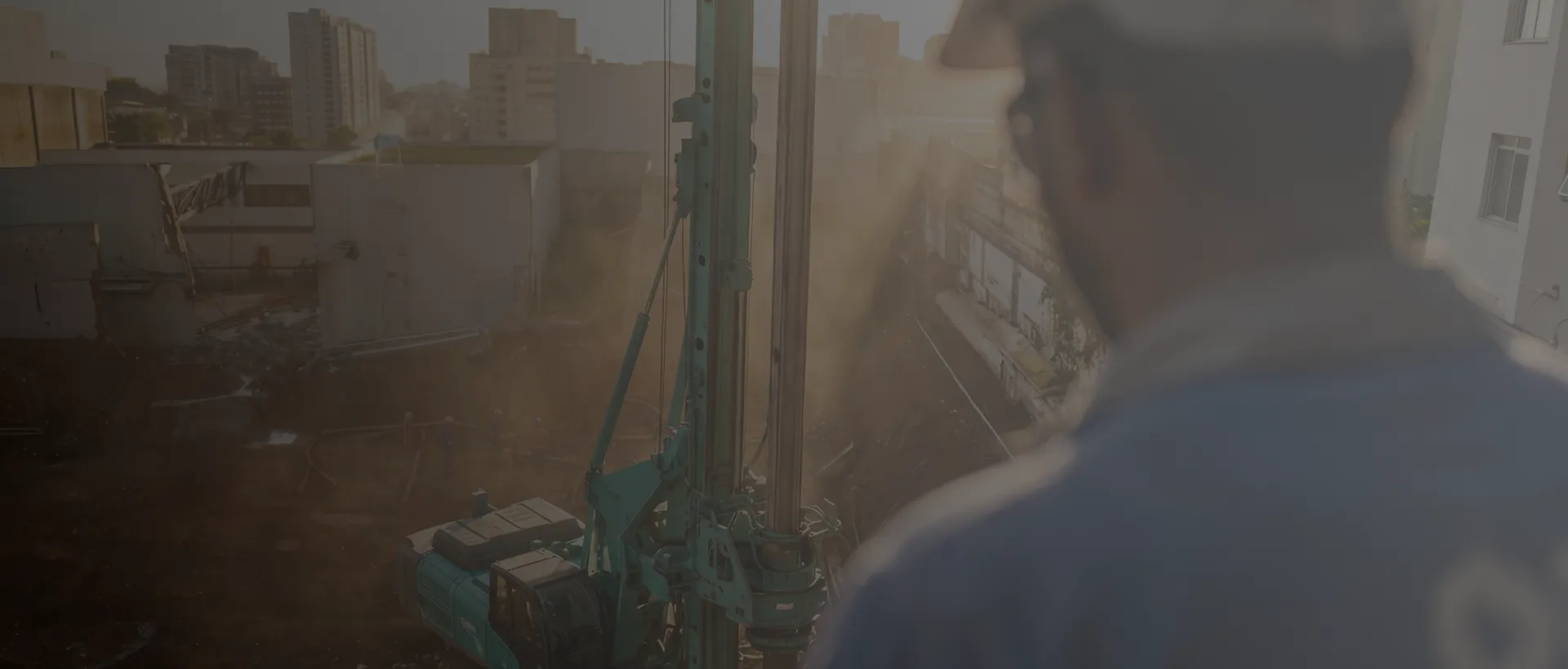 Engenheiro observando instalação de equipamento de perfuração em canteiro de obras ao entardecer